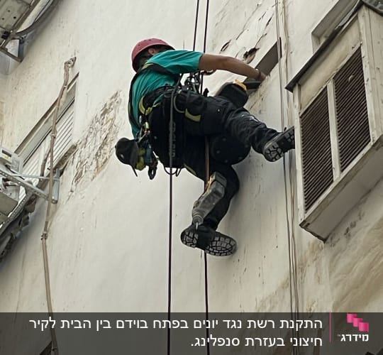 אדם עם קסדה מטפס על קיר בעזרת חבלים